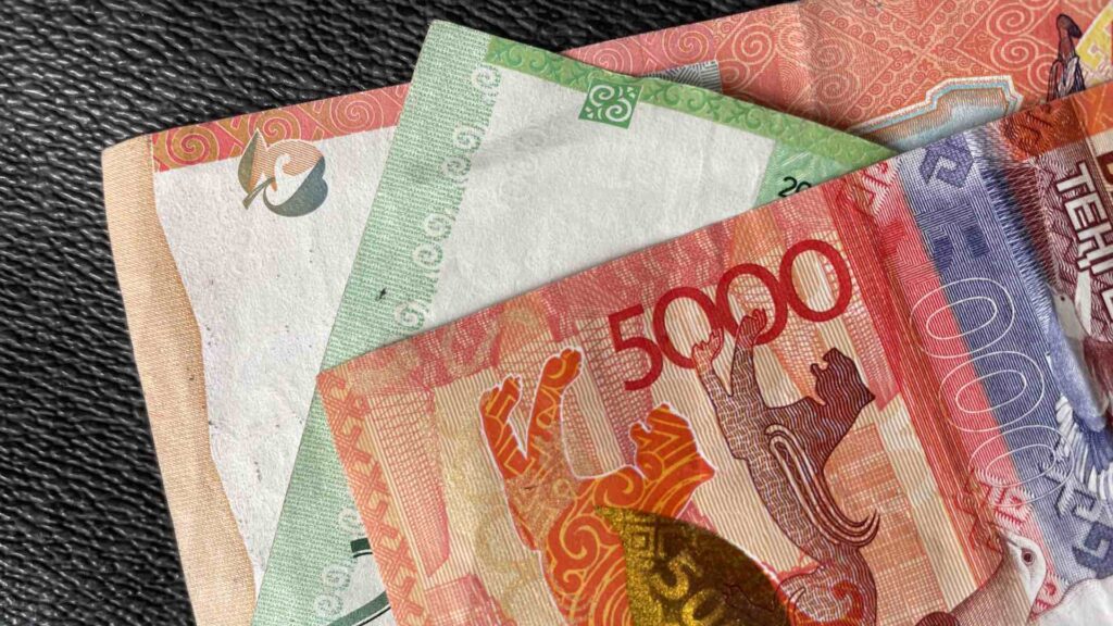 Тенге лежит на черной кожаной поверхности
