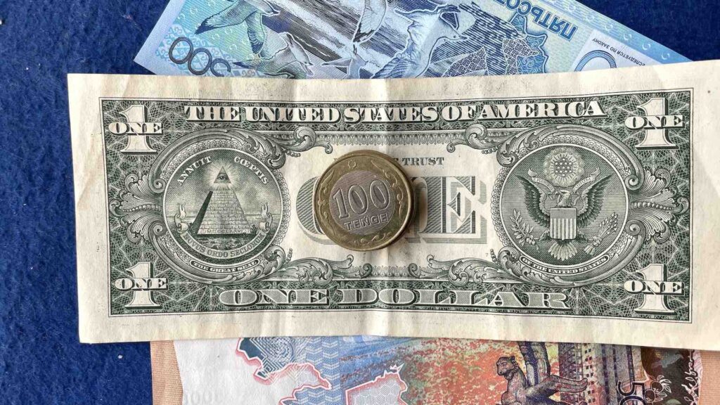 Монеты 100 тенге на купюрах в 500 и 500 тенге и 1 доллар