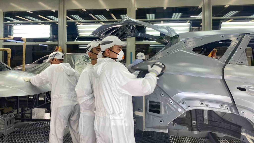 Работники завода шлифуют каркас автомобиля
