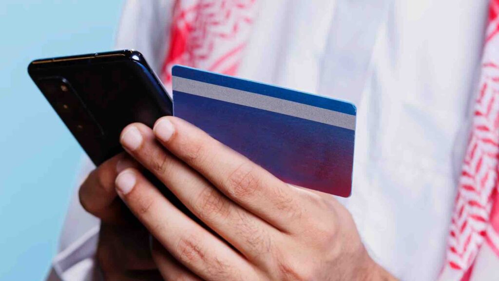Мусульманин держит в руке банковскую карту и смартфон - исламский банкинг